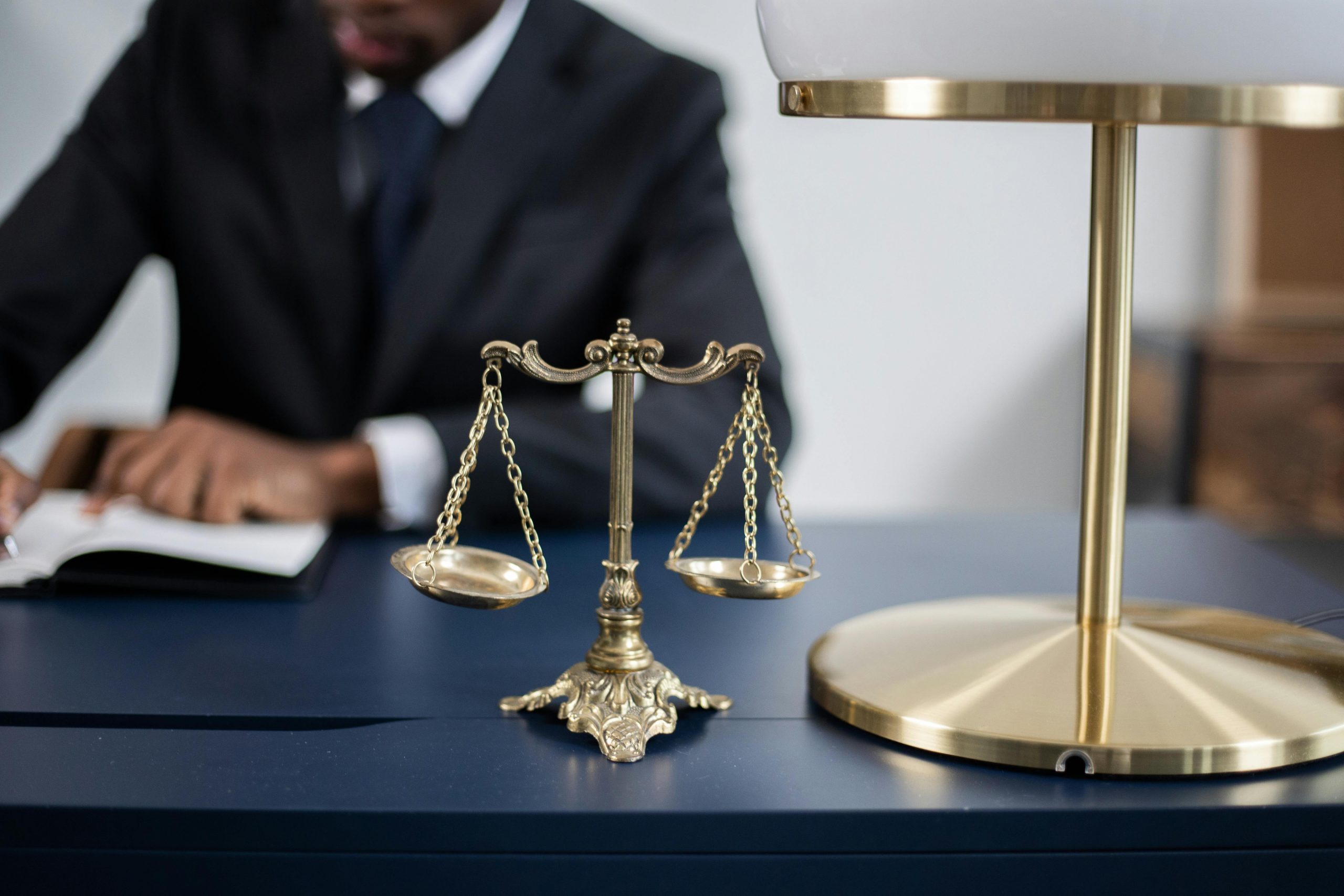 male lawyer writing at a desk with a small decorative justice scale figurine