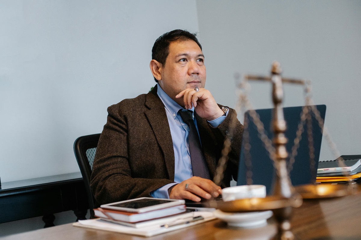 lawyer sitting at a desk, looking thoughtful, with a laptop and a justice-themed weighing scale figurine nearby